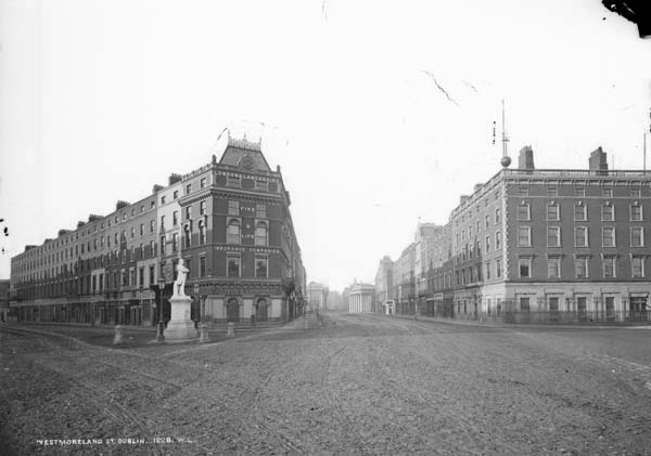 Westmoreland St., Dublin City, Co. Dublin, photographed by Robert French. From the National Library of Ireland's Lawrence Photograph Collection. The view represents a southward look down Westmoreland Street from O'Connell (Carlisle) Bridge. To the left, stretching southeast, is D'Olier Street. Between the two streets is the "central plot directly opposite the bridge" that Christine Casey describes as "the single most conspicuous site in the city" (Casey 422).